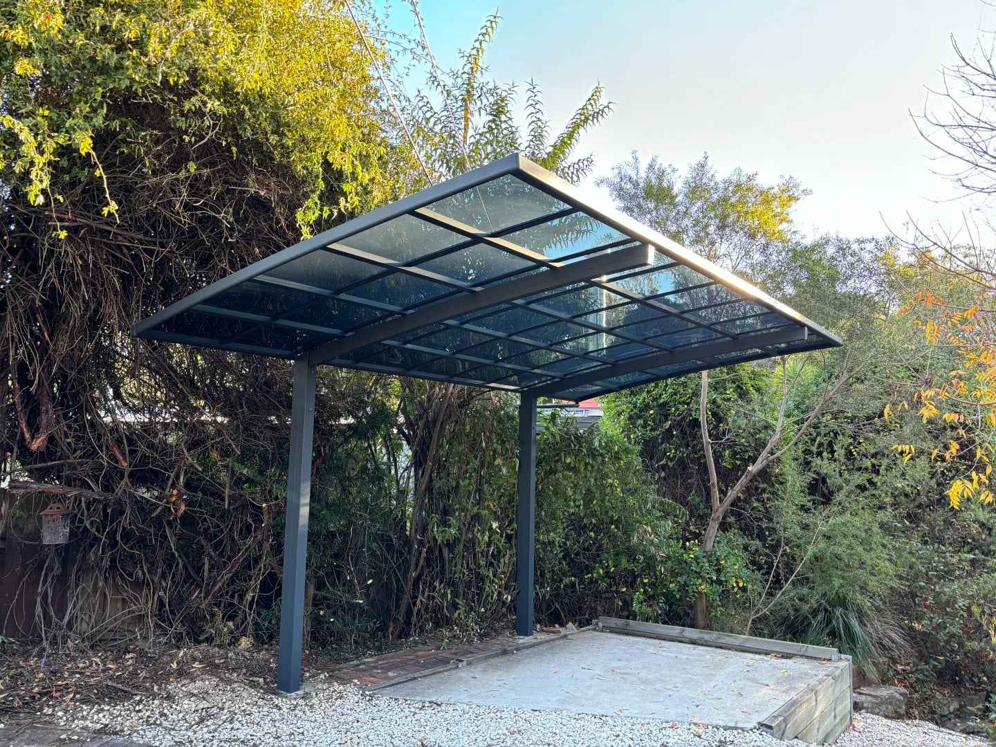 Modern outdoor carport awning with glass roof by Kings Awning, set among green trees